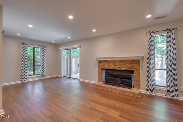 an empty room with wooden floor fireplace and windows