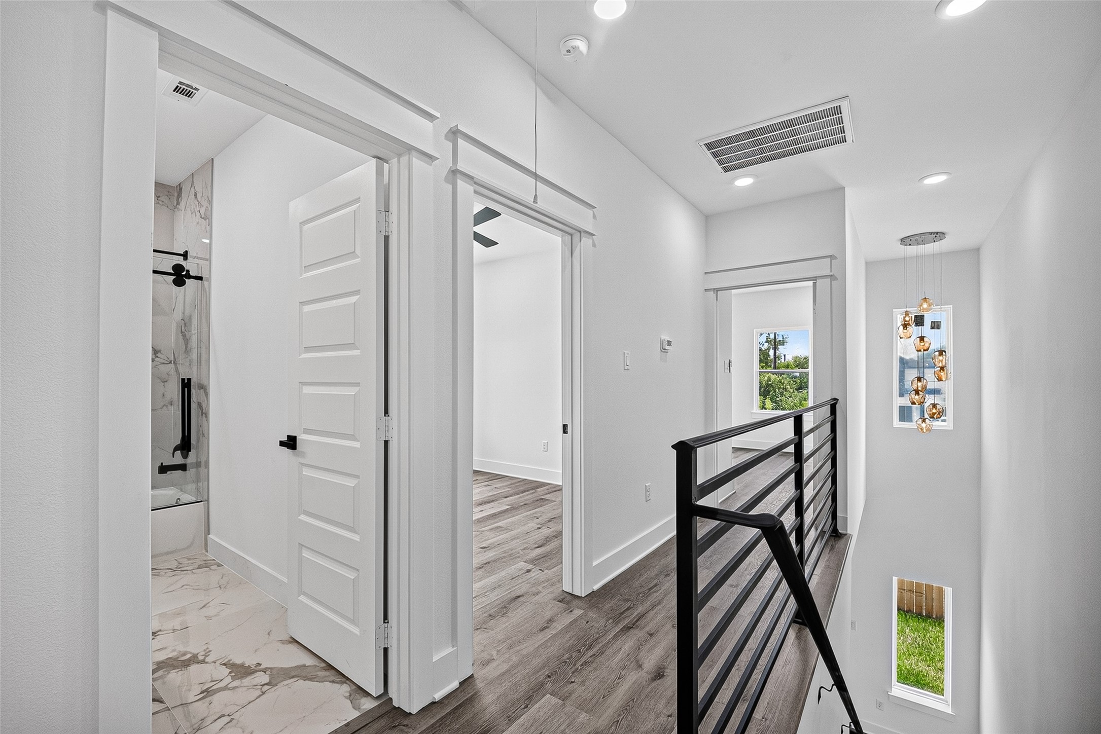 6747 Liverpool Street Houston, TX 77021 - Photo 19 of 38 An upper hallway with wood-look plank flooring leads to multiple bedrooms, a full bathroom, and a staircase accented by a sleek metal railing.