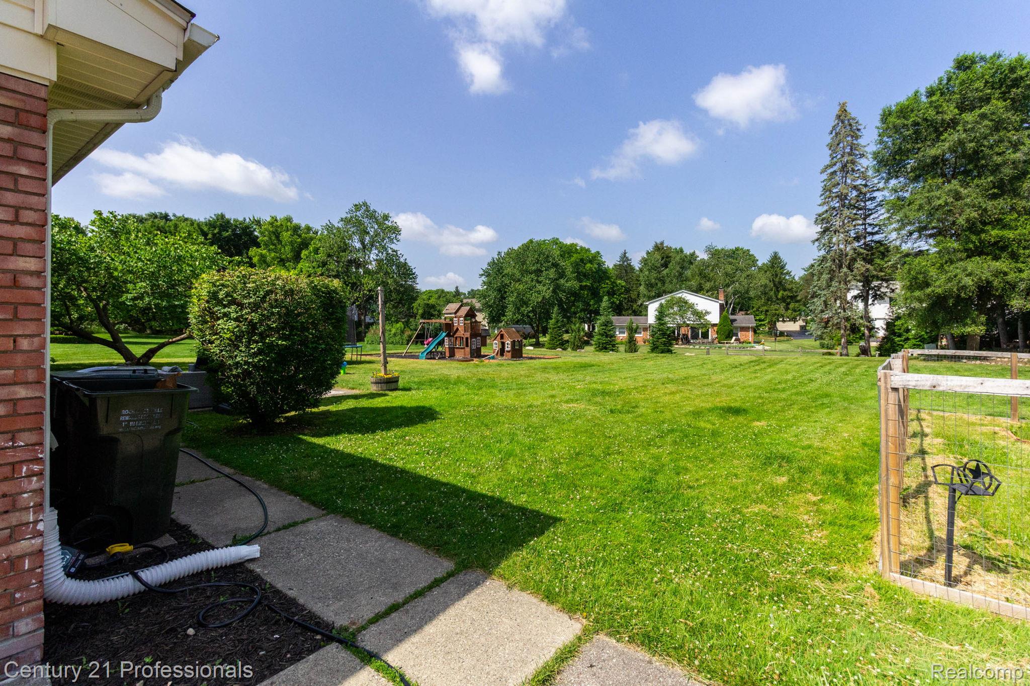 671 Bridgestone Drive Rochester, MI 48309 - Photo 44 of 50 Expansive green lawn with mature trees and a wooden fence defining one border