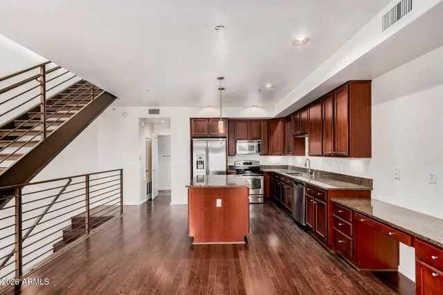 a kitchen with stainless steel appliances granite countertop a stove top oven a refrigerator a sink and dishwasher with wooden floor