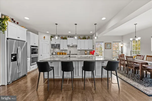 a kitchen with stainless steel appliances kitchen island granite countertop a dining table chairs and wooden floor