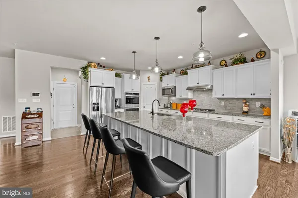 a kitchen with stainless steel appliances kitchen island granite countertop a dining table chairs and white cabinets