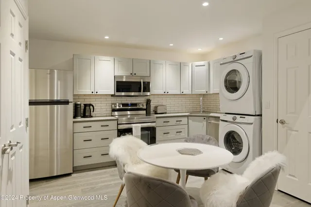 a kitchen with stainless steel appliances granite countertop a stove a sink a refrigerator and white cabinets with wooden floors