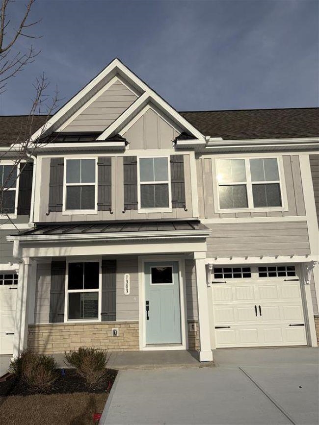 View of front of home with an attached garage, a porch, driveway, stone siding, and board and batten siding