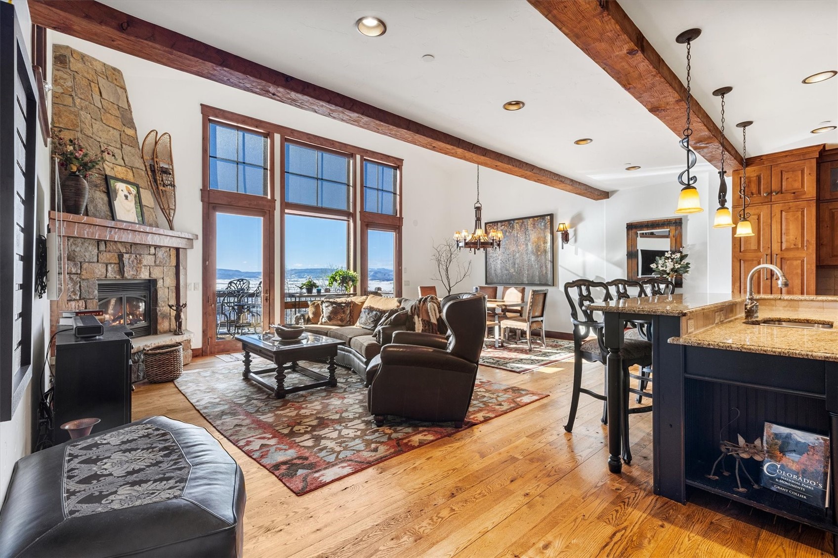 2324 Glacier Ridge, Unit B Steamboat Springs, CO 80487 - Photo 7 of 46 Living room with light wood-style flooring, beam ceiling, a stone fireplace, a mountain view, and a chandelier