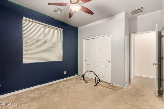 an empty room with a chandelier fan and kitchen view