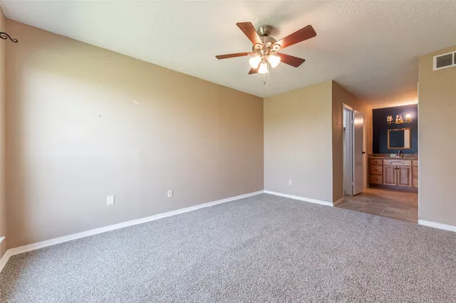 an empty room with chandelier fan and a kitchen view