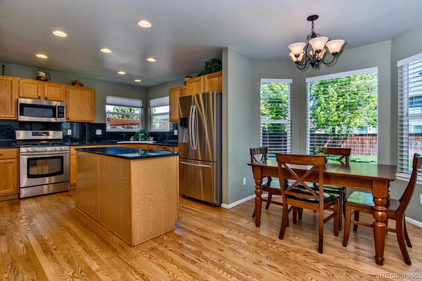 1757 Spring Water Place Highlands Ranch, CO 80129 - Photo 8 of 34 a kitchen with stainless steel appliances granite countertop a stove refrigerator a dining table and chairs with wooden floor