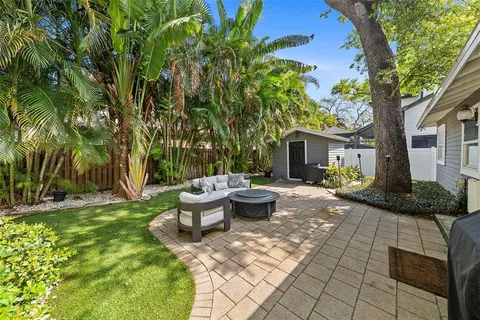 a view of a backyard with table and chairs potted plants and large tree