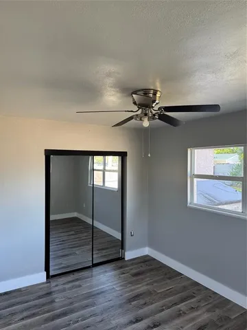 an empty room with wooden floor fan and windows