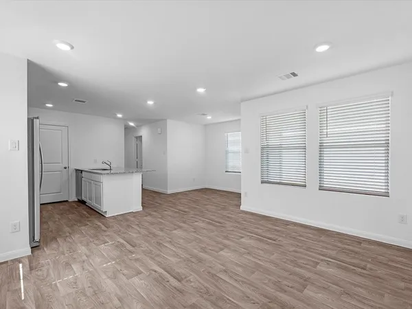a view of an empty room with kitchen and window