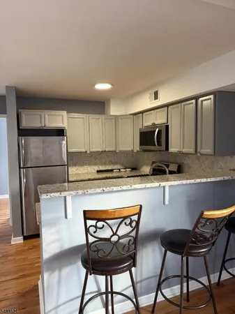 a kitchen with stainless steel appliances granite countertop a refrigerator a stove a sink dishwasher and white cabinets with wooden floor