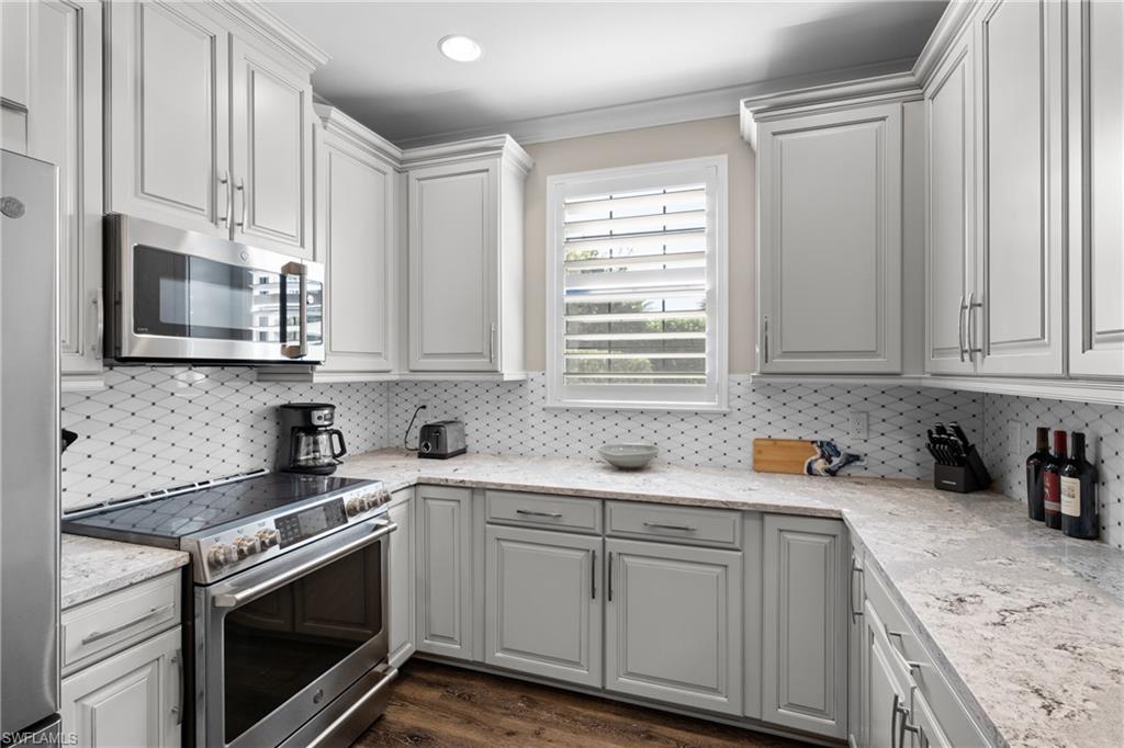 9684 Montelanico Loop, Unit 101 Naples, FL 34119 - Photo 11 of 49 Kitchen with white cabinets, dark hardwood / wood-style flooring, appliances with stainless steel finishes, and tasteful backsplash