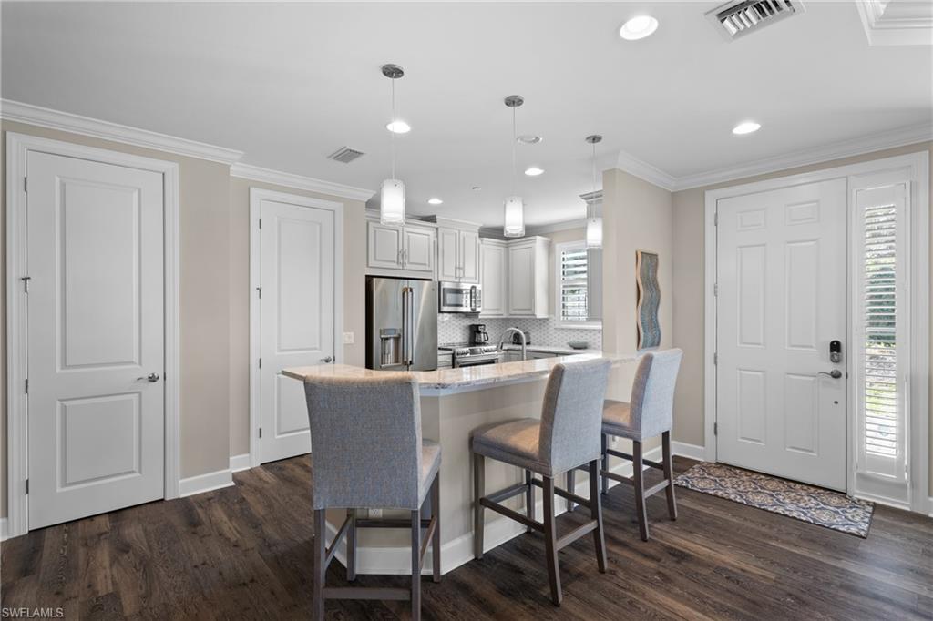 9684 Montelanico Loop, Unit 101 Naples, FL 34119 - Photo 8 of 49 Kitchen featuring a kitchen breakfast bar, light stone counters, appliances with stainless steel finishes, decorative light fixtures, and dark hardwood / wood-style flooring