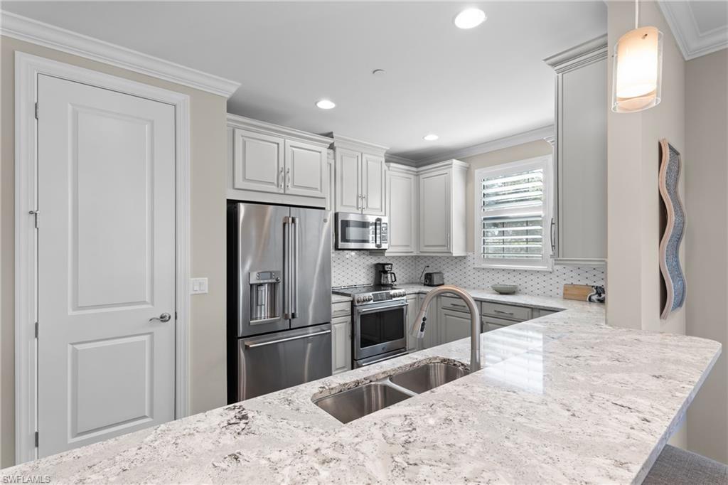 9684 Montelanico Loop, Unit 101 Naples, FL 34119 - Photo 9 of 49 Kitchen with sink, crown molding, hanging light fixtures, kitchen peninsula, and stainless steel appliances