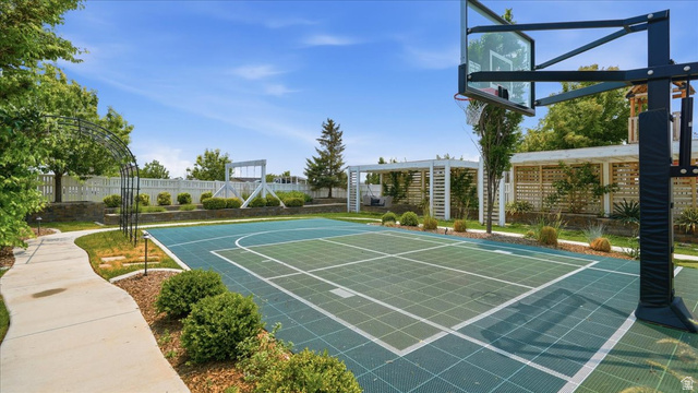 2038 East Ranch Road Eagle Mountain, UT 84005 - Photo 47 of 66 Outdoor sports court with a basketball hoop, surrounded by landscaped garden beds, a winding concrete pathway, a decorative metal archway, and white lattice privacy fencing