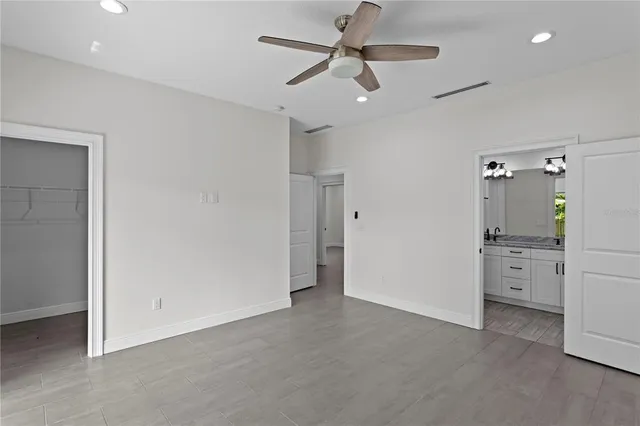 an empty room with chandelier fan and kitchen view