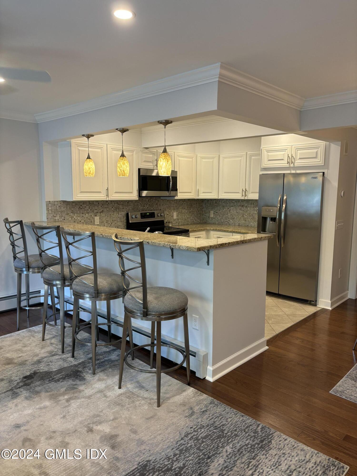 1465 East Putnam Avenue, Unit 306 Riverside, CT 06878 - Photo 2 of 13 a kitchen with stainless steel appliances kitchen island granite countertop a table chairs in it and wooden floors