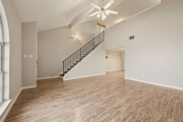 a view of an empty room with wooden floor and a ceiling fan
