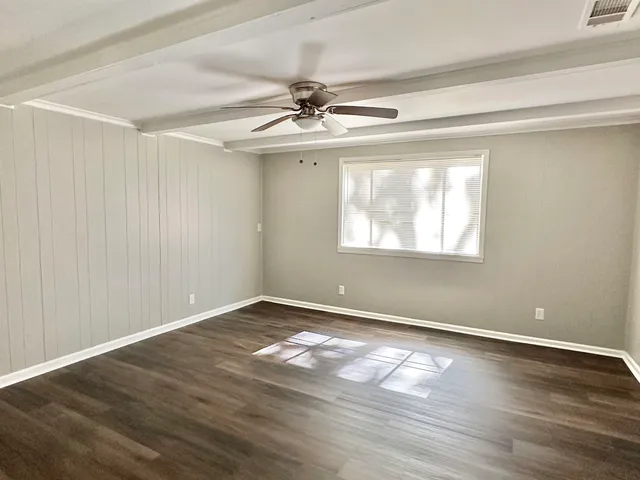 an empty room with wooden floor chandelier fan and windows