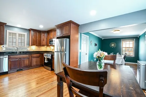 a kitchen with stainless steel appliances kitchen island granite countertop a refrigerator a stove a sink a dining table and chairs with wooden floor