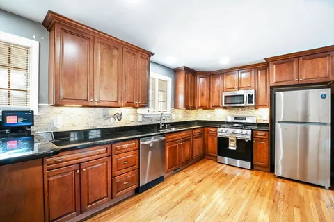 a kitchen with stainless steel appliances granite countertop a refrigerator a sink dishwasher a stove with wooden cabinets and floor