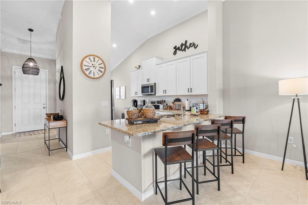 9402 Pocida Court, Unit 202 Naples, FL 34119 - Photo 13 of 31 Kitchen with white cabinetry, light stone counters, a breakfast bar area, pendant lighting, and a peninsula