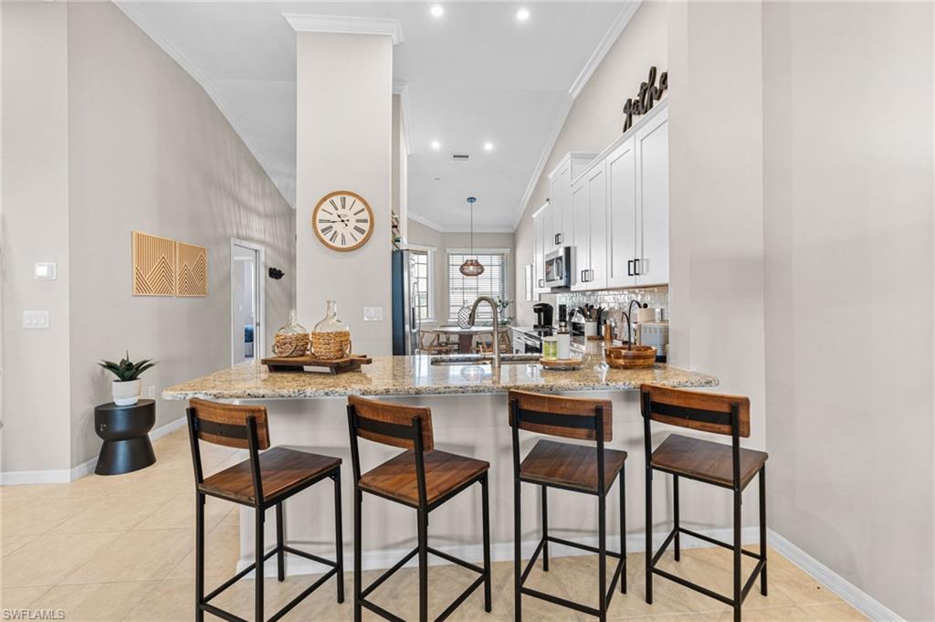 9402 Pocida Court, Unit 202 Naples, FL 34119 - Photo 14 of 31 Kitchen with a breakfast bar area, light stone counters, white cabinetry, decorative light fixtures, and a peninsula