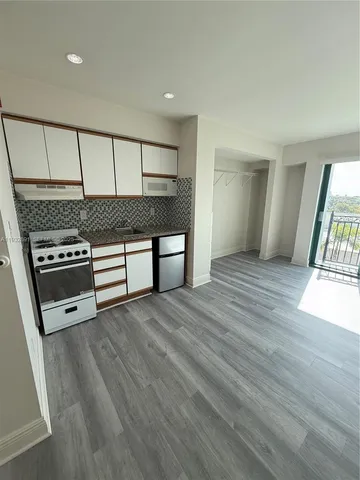 an empty room with wooden floor kitchen view and windows