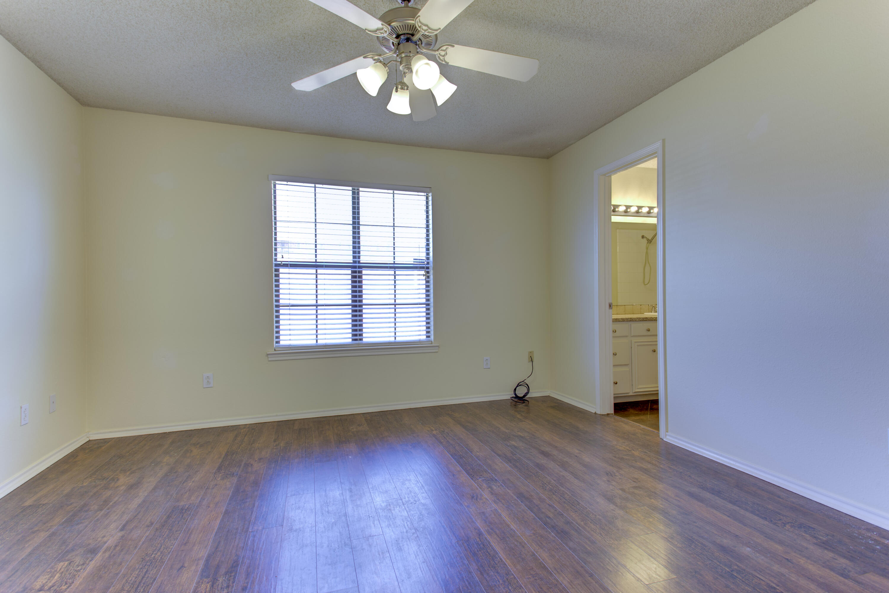 6804 7th Street Lubbock, TX 79416 - Photo 13 of 42 an empty room with wooden floor chandelier fan and windows