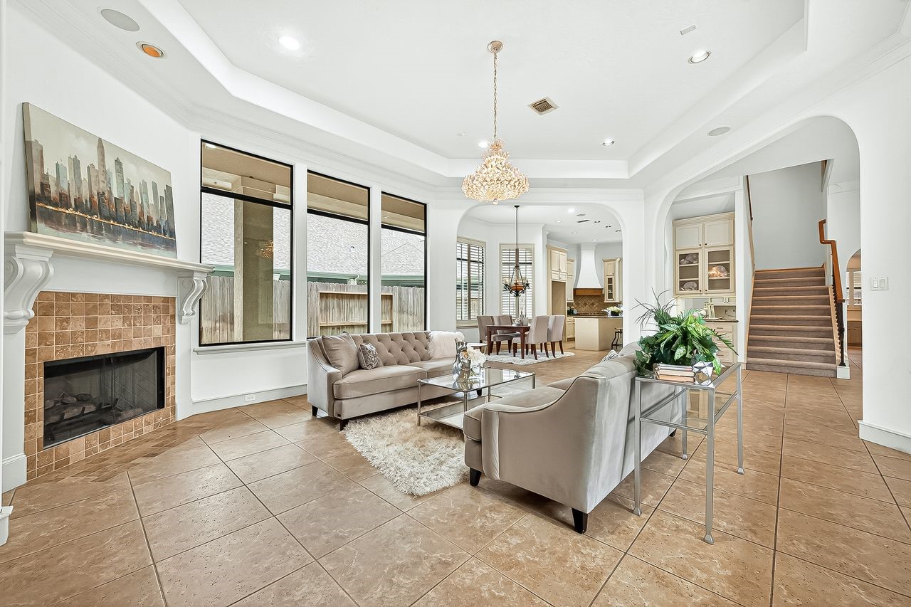 16610 Champagne Falls Court Spring, TX 77379 - Photo 4 of 50 Grand living room showcases a magnificent chandelier, luxurious drapes, tiled flooring, media built-ins & a gas log fireplace—all overlooking your stunning pool oasis.