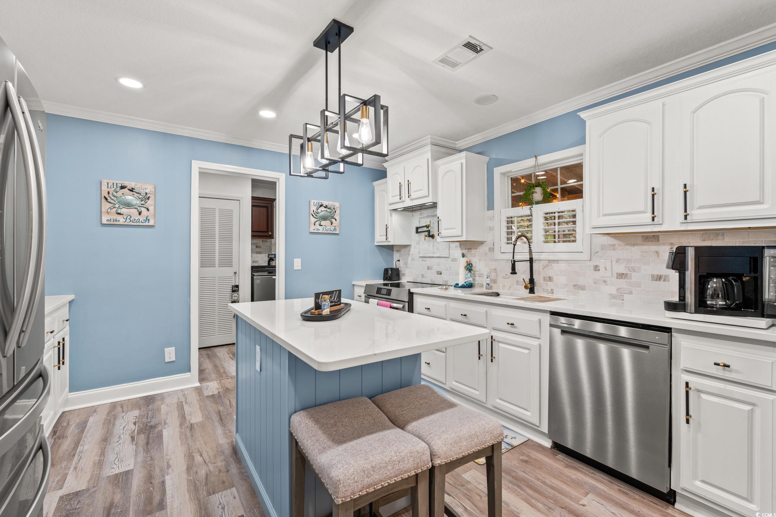 90 Offshore Drive Murrells Inlet, SC 29576 - Photo 3 of 40 Kitchen with white cabinets, appliances with stainless steel finishes, decorative light fixtures, a kitchen breakfast bar, and light wood-style floors