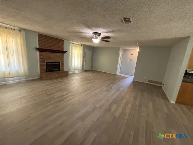 an empty room with wooden floor fireplace and windows