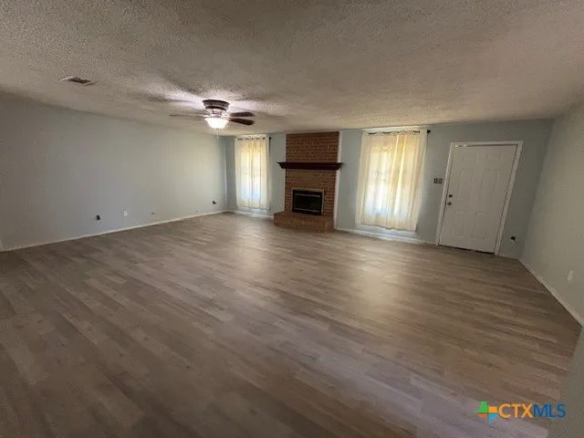 an empty room with wooden floor ceiling fan and windows