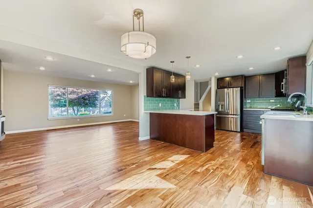 a kitchen with stainless steel appliances kitchen island granite countertop a refrigerator and a wooden floors