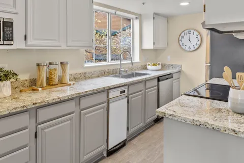 a kitchen with granite countertop a sink a stove a clock and cabinets