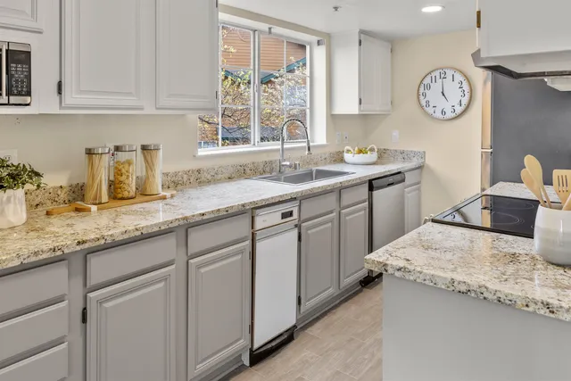 a kitchen with granite countertop a sink a stove a clock and cabinets