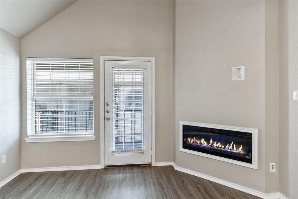6108 Abrams Road, Unit 521 Dallas, TX 75231 - Photo 2 of 20 Modern living space featuring an inset electric fireplace, wood-finish flooring, a vaulted ceiling, a glass-paned door, and a large window with blinds