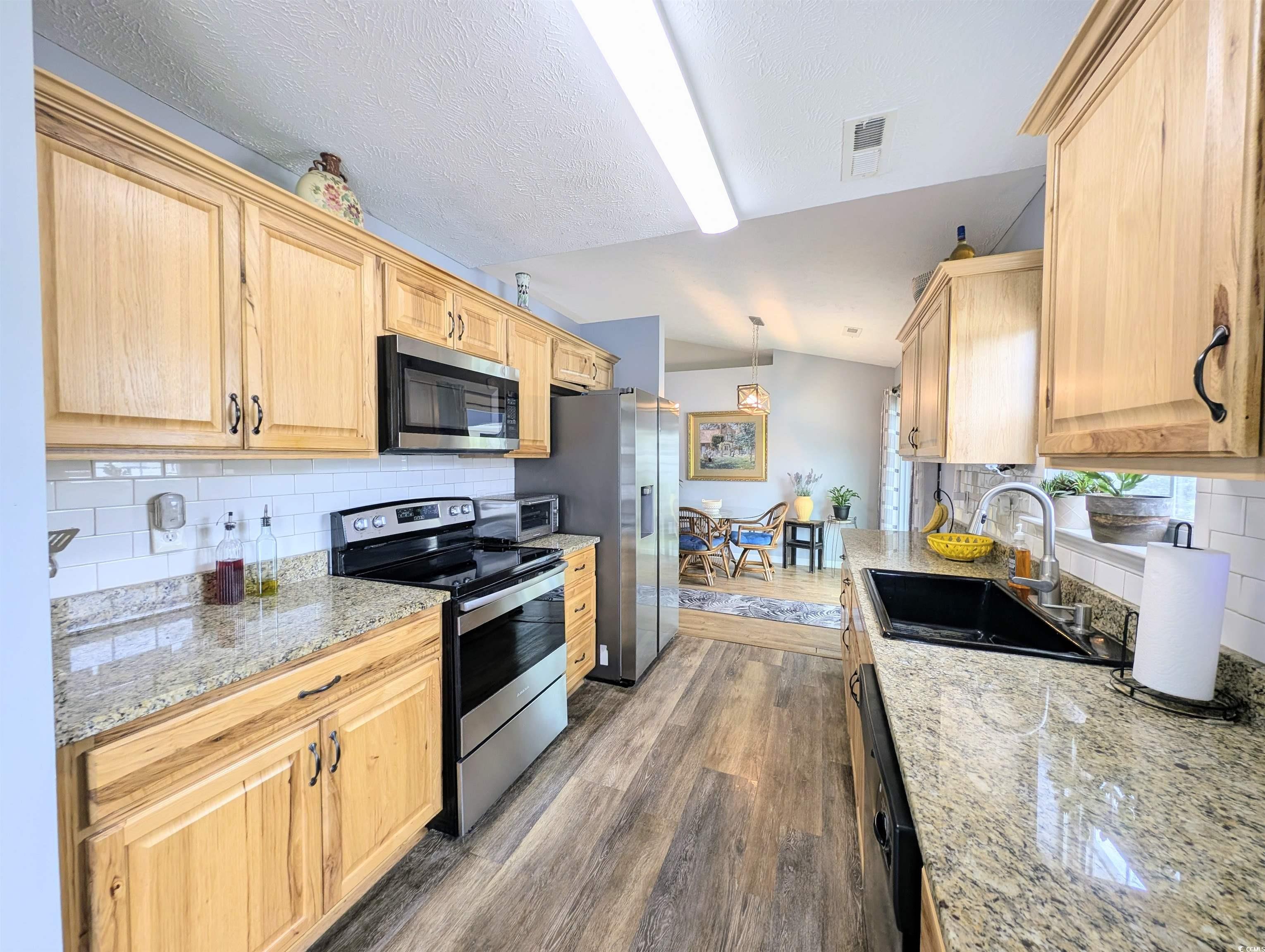 1013 Autumn Drive Murrells Inlet, SC 29576 - Photo 15 of 36 Galley kitchen with tasteful backsplash, stainless steel appliances, dark wood-style flooring, hanging light fixtures, and a textured ceiling
