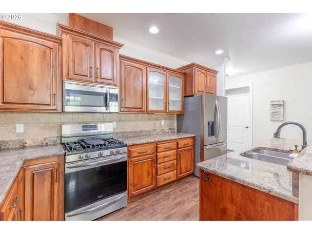 a kitchen with stainless steel appliances granite countertop a stove a sink dishwasher a refrigerator and wooden cabinets with wooden floor