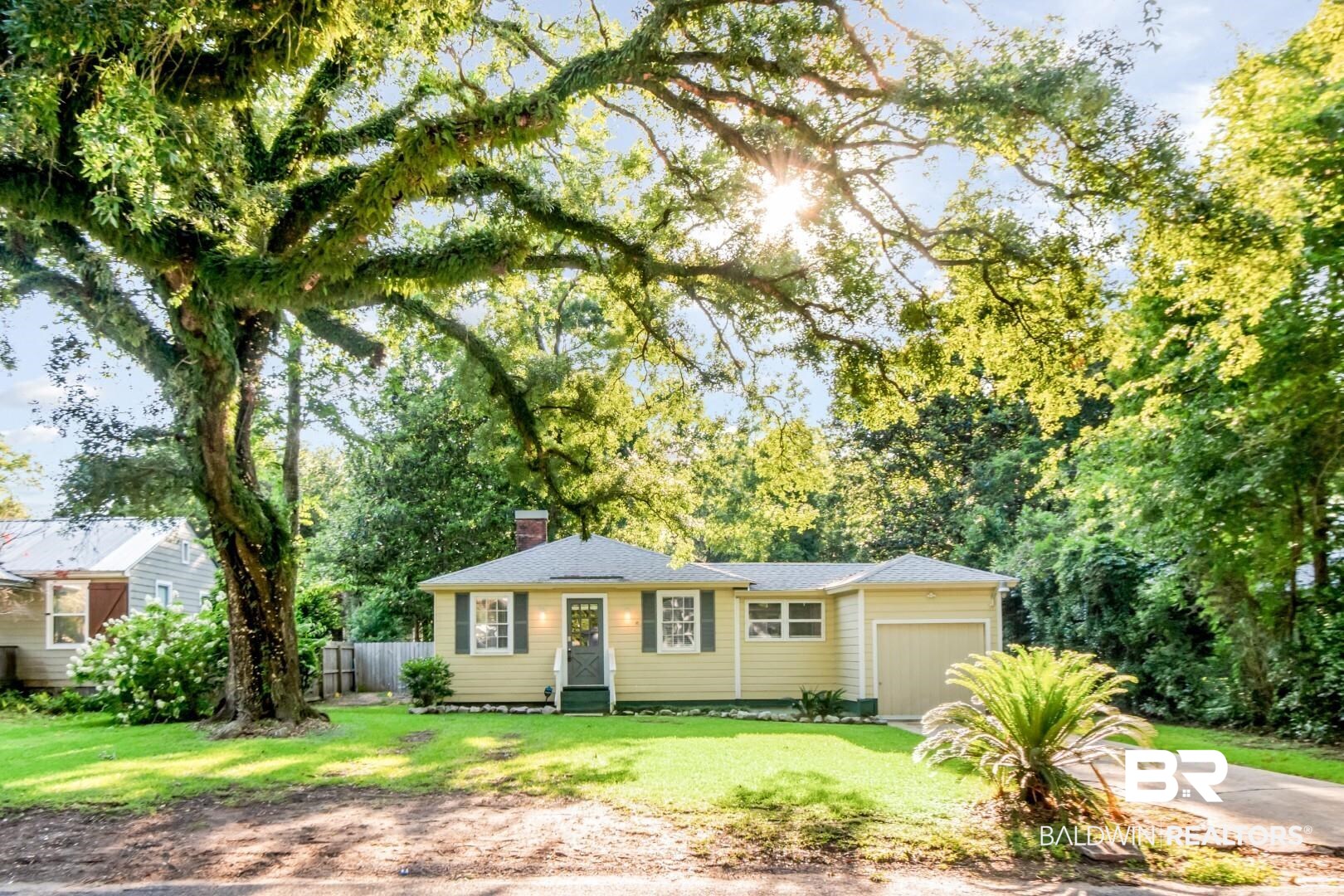 263 Border Drive East Mobile, AL 36608 - Photo 1 of 27 Charming single-story residence with an attached garage, featuring a light yellow exterior, dark green shutters, and a prominent chimney