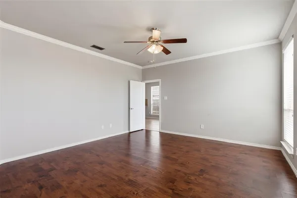 an empty room with wooden floor ceiling fan and windows
