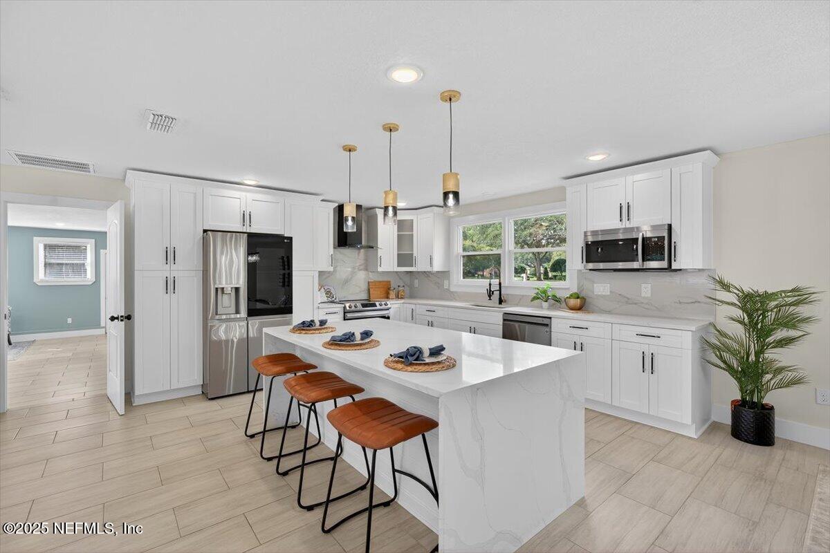10779 Scott Mill Road Jacksonville, FL 32223 - Photo 10 of 82 a white kitchen with stainless steel appliances kitchen island granite countertop a refrigerator a sink dishwasher a stove a dining table and chairs with wooden floor