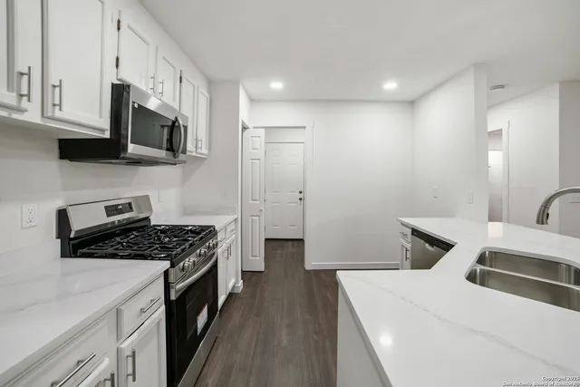 a kitchen with stainless steel appliances a white stove top oven a sink a refrigerator white cabinets and wooden floor