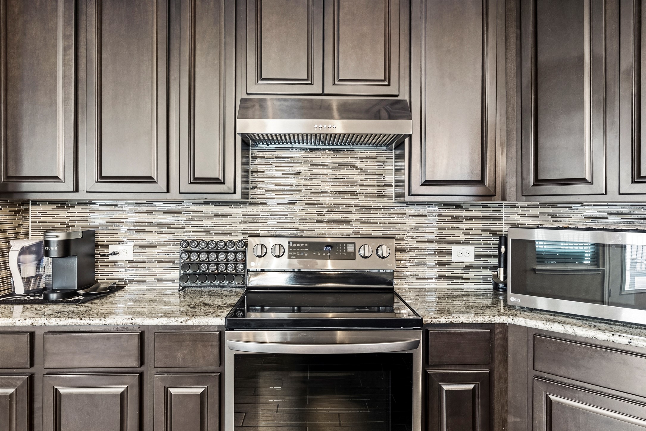 105 West Point Way Elgin, TX 78621 - Photo 5 of 27 Kitchen featuring dark wood cabinetry, stainless steel appliances, a mosaic tile backsplash, and granite countertops