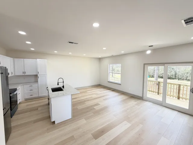 a kitchen with stainless steel appliances kitchen island granite countertop a stove a sink a refrigerator white cabinets and wooden floor