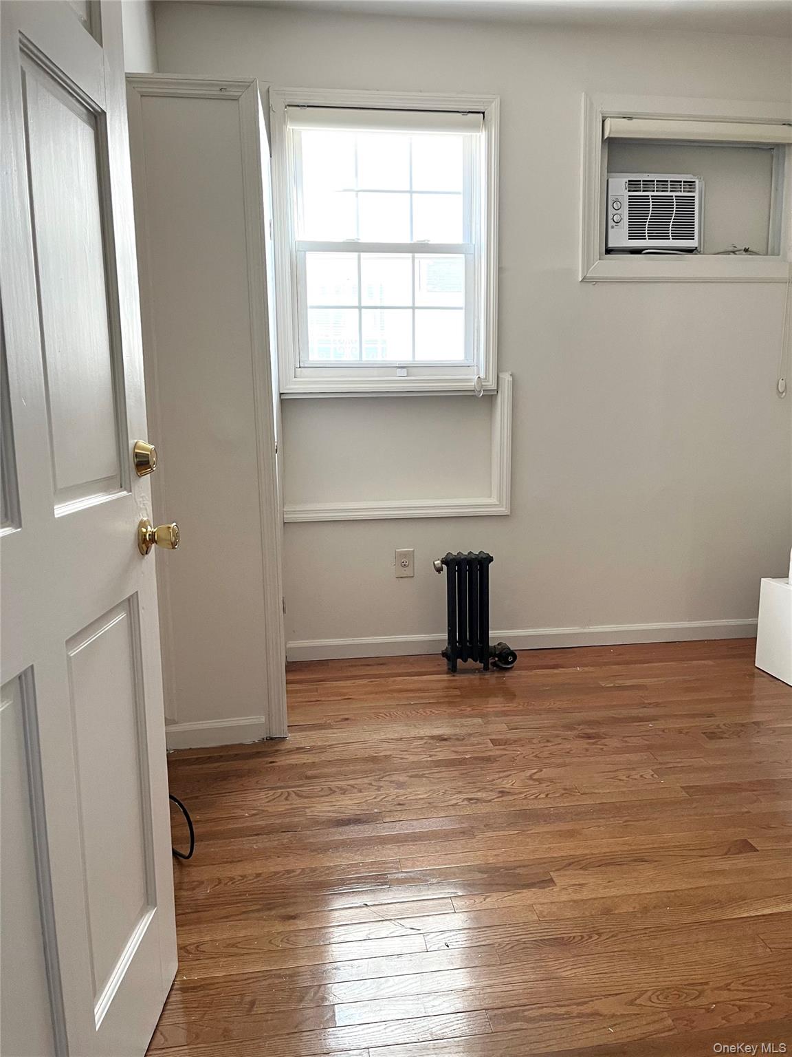 107-33 115th Street Queens, NY 11419 - Photo 3 of 5 a view of an empty room with a window and wooden floor