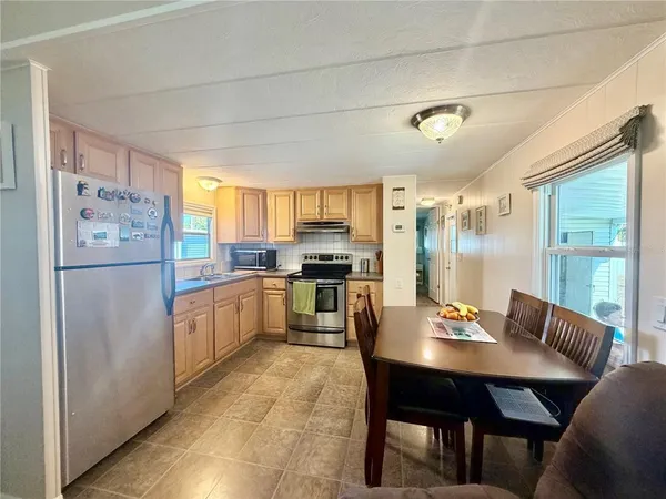 a kitchen with stainless steel appliances granite countertop a refrigerator a sink dishwasher a dining table and chairs with wooden floor