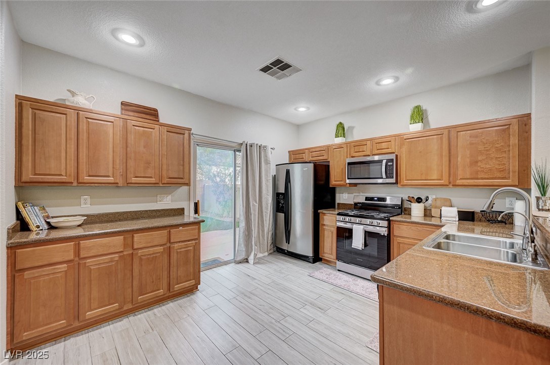 9310 Pinarello Street Las Vegas, NV 89178 - Photo 15 of 61 Kitchen with stainless steel appliances, dark stone countertops, light wood-type flooring, recessed lighting, and brown cabinetry