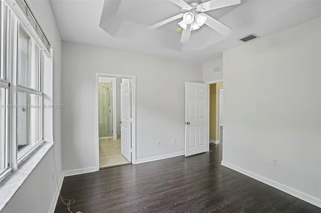 an empty room with wooden floor fan and windows